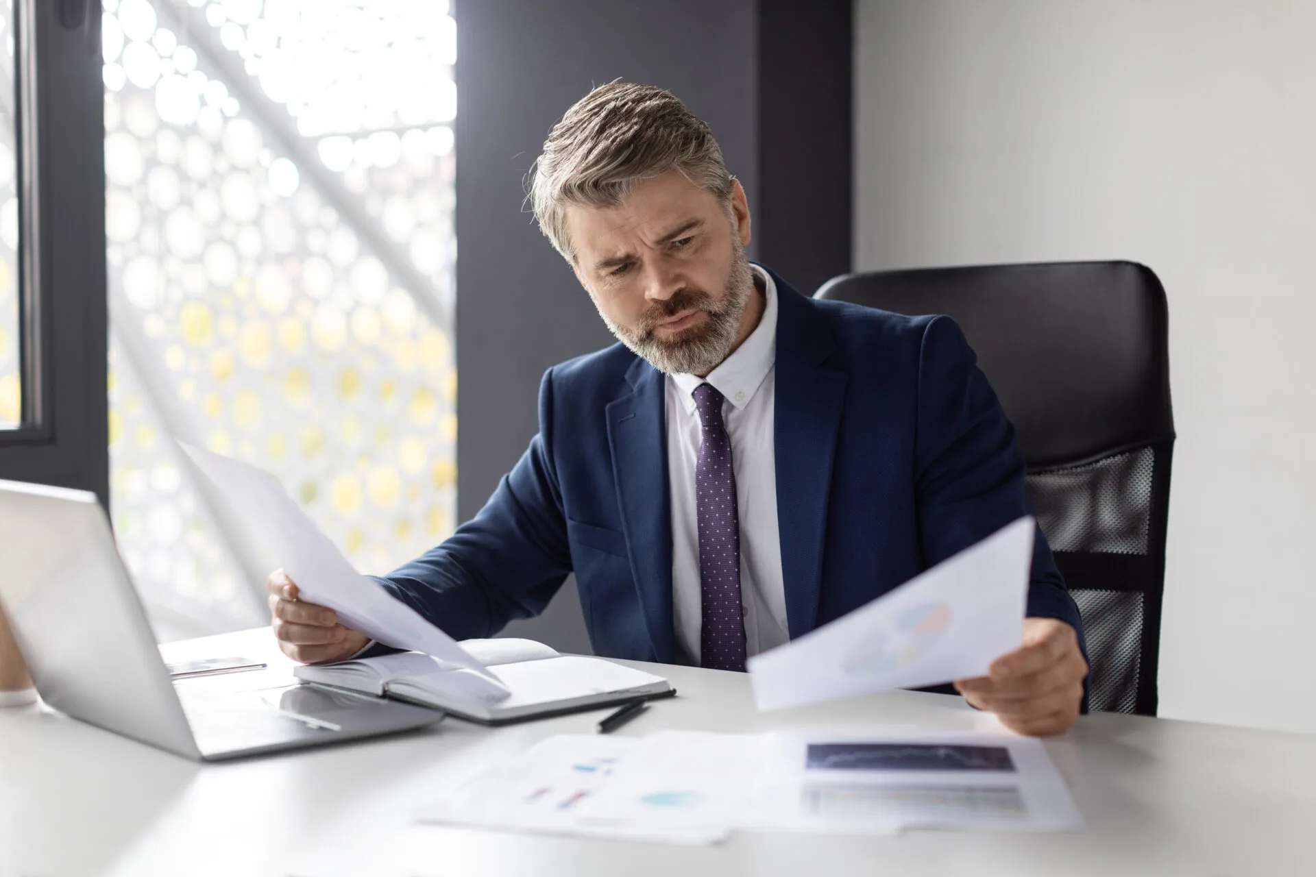 Thoughtful Mature Businessman Working With Papers At Desk In Modern Office